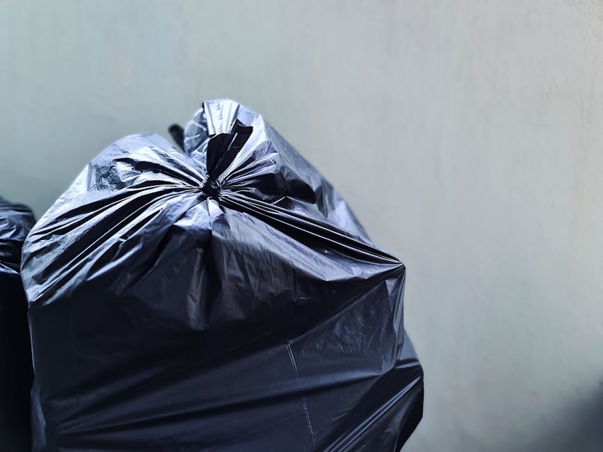 A large, open area of land filled with various types of waste and debris, including scattered plastic bottles, paper, and small fragments of refuse. Several small tractors or mini-dump trucks, painted